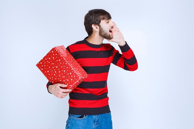 빨간색 선물 상자를 들고 그것을 배달 할 누군가를 호출하는 빨간색 줄무늬 셔츠에 남자.