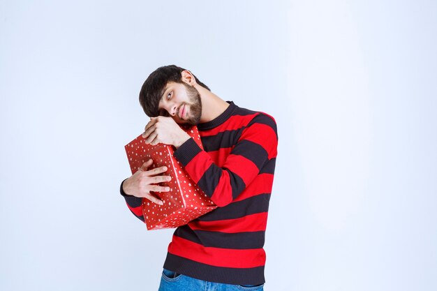 빨간색 선물 상자를 들고 꽉 껴안고 다른 사람과 공유하고 싶지 않은 빨간색 줄무늬 셔츠를 입은 남자.