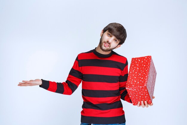 Man in red striped shirt holding a red gift box and looks confused and thoughtful.