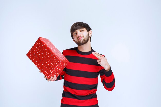 Uomo in camicia a righe rosse che tiene una confezione regalo rossa e la promuove.