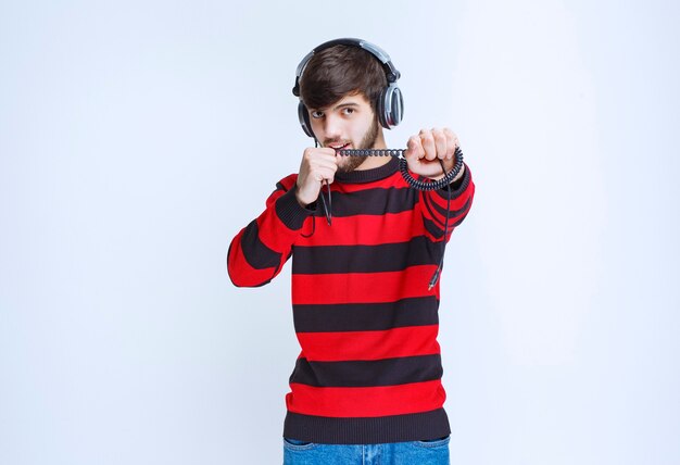 헤드폰을 듣고 스마트 폰의 자신의 재생 목록에서 음악을 설정하는 빨간 줄무늬 셔츠를 입은 남자.