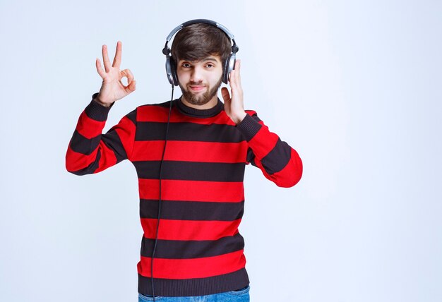 Uomo in camicia a righe rossa che ascolta le cuffie e mostra il segno di divertimento.