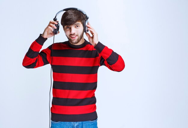 Man in red striped shirt taking off the headphones to hear outer voices.