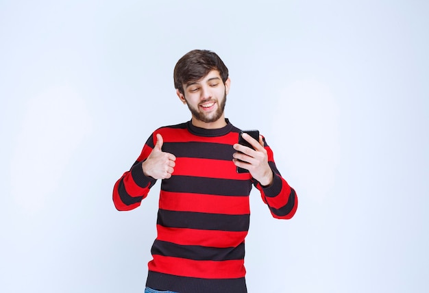 Man in red striped shirt talking to the phone and showing thumb up as hearing good news.
