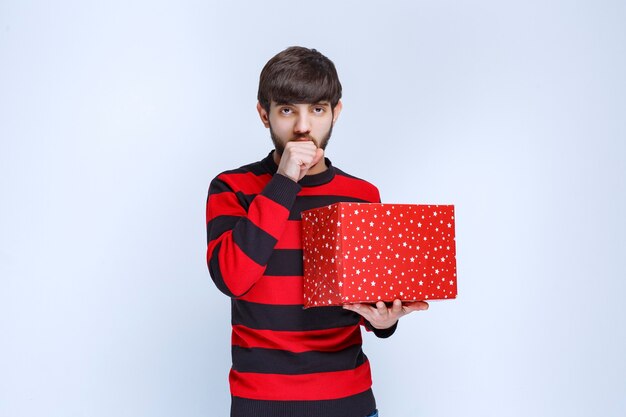 Man in red striped shirt with a red gift box looks confused and thoughtful.