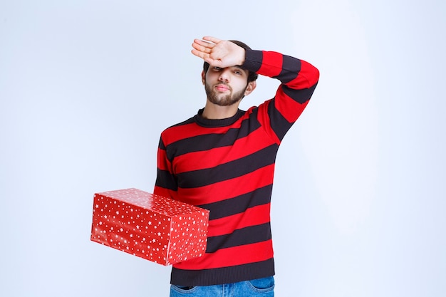 Man in red striped shirt with a red gift box looks sleepy and exhausted.