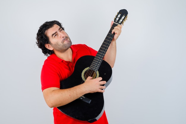 man in red t-shirt playing guitar and looking pensive