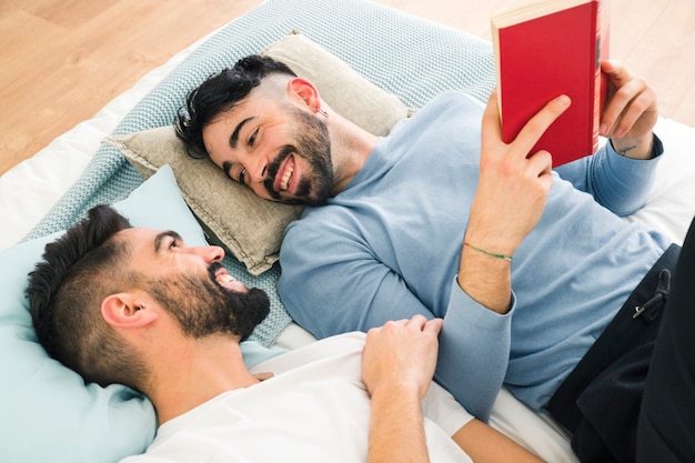 Man relaxing on bed holding book in hand looking at his boyfriend