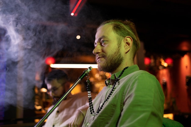 Free photo man relaxing by vaping from a hookah in a bar