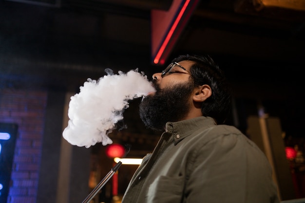 Man relaxing by vaping from a hookah in a bar