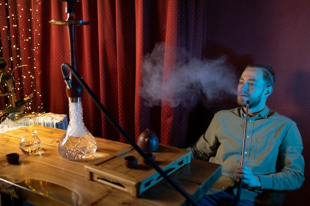 Man relaxing by vaping from a hookah in a bar