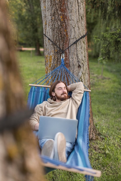 Man relaxing in hammock while working on laptop