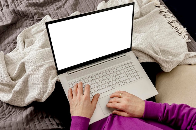 Человек расслабляется на кровати и держит портативный компьютер. макет с пустым белым экраном. человек использует ноутбук для серфинга в интернете, чтения новостей, просмотра фильмов, учебы или работы в интернете. приложение, игра, презентация веб-сайта
