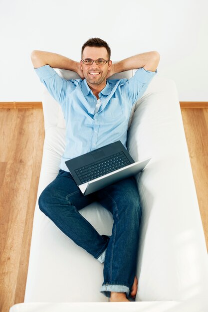 Man relaxing on sofa with laptop and hand behind head