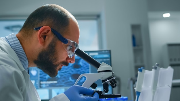 Man research scientist looking at samples under microscope in modern equipped laboratory