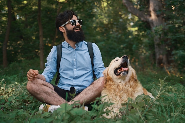 Человек отдыхает на траве, сидя со скрещенными ногами со своей собакой