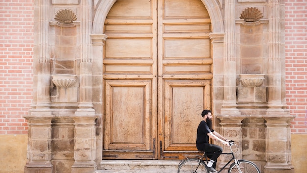 A man riding the bicycle in front of an antique closed door