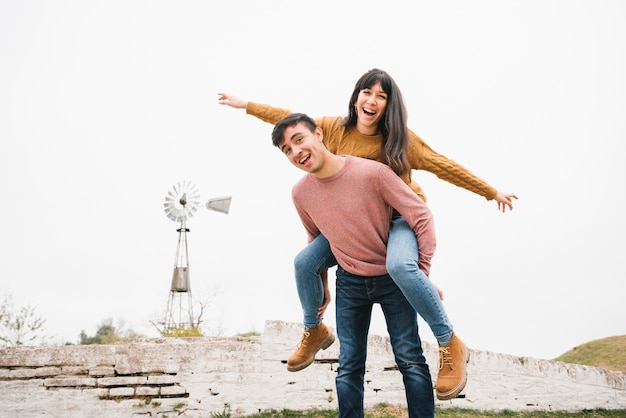 Free photo man riding laughing woman piggyback having fun in nature