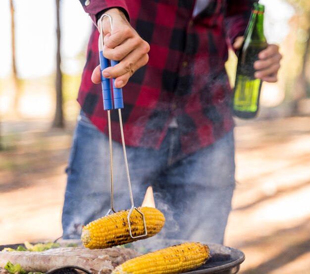 Man roasting corn on barbecue while drinking beer