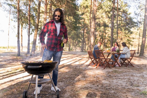 Man roasting corn on barbecue while friends converse at table