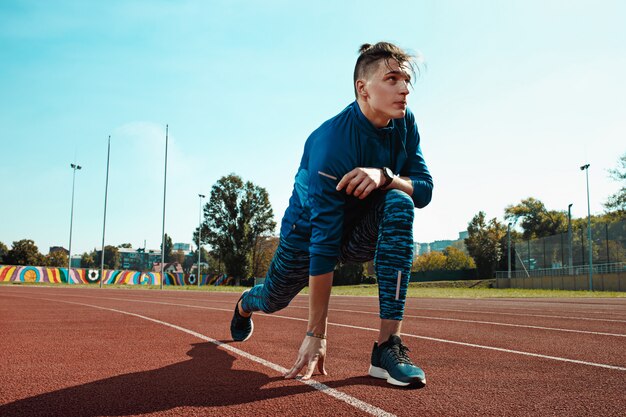 Man runner stretching legs preparing for run training on stadium tracks doing warm-up