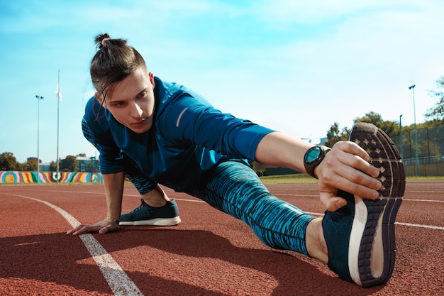 Man runner stretching legs preparing for run training on stadium tracks doing warm-up