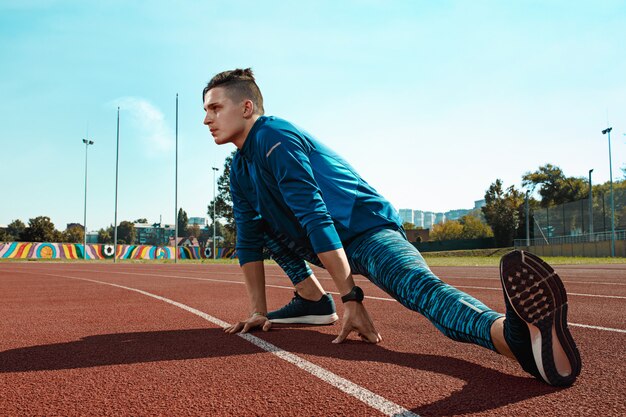 ウォーミングアップを行うスタジアムトラックで実行トレーニングの準備をして足を伸ばし男ランナー