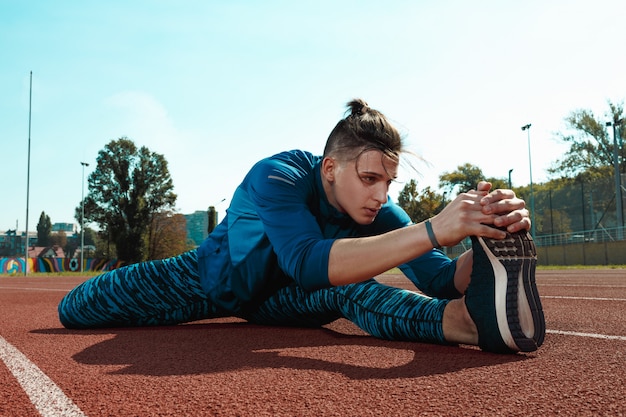 Man runner stretching legs preparing for run training on stadium tracks doing warm-up