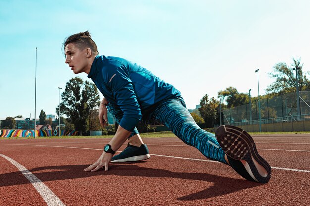 Man runner stretching legs preparing for run training on stadium tracks doing warm-up
