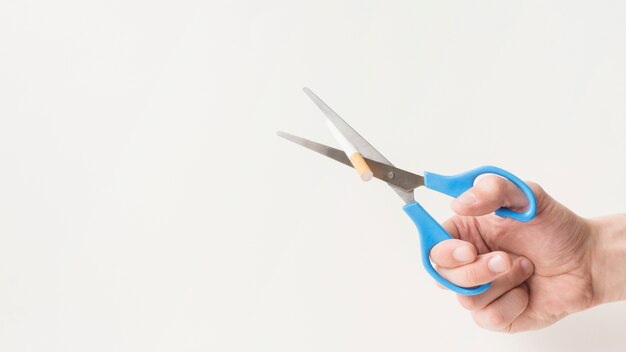 Man's hand cuts a cigarette with scissor on white surface