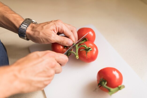 Man's hand cutting tomatoes on chopping board