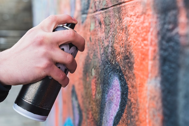 La mano dell'uomo che disegna i graffiti sulla parete con la latta dell'aerosol