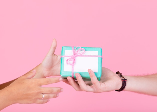 Man's hand giving gift box to other person against pink background