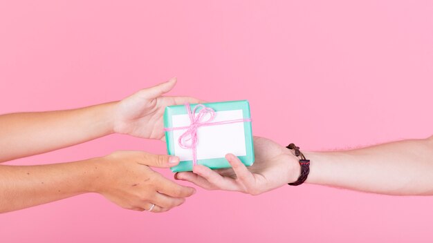 Man's hand giving gift to her woman against pink background