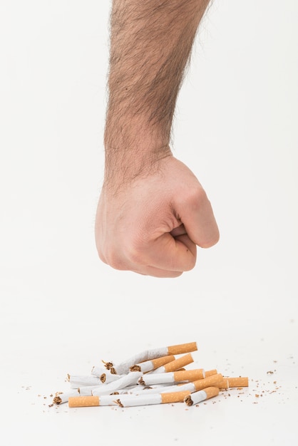 A man's hand giving punch to the broken cigarettes isolated on white backdrop