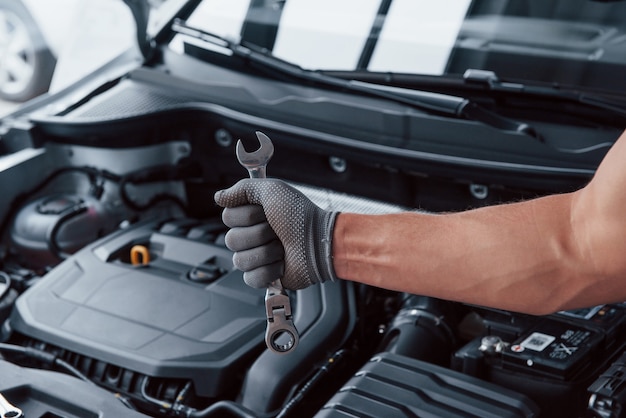 Free photo man's hand in glove holds wrench in front of broken automobile