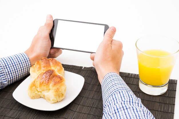 Man's hand holding cell phone with blank white screen at breakfast time