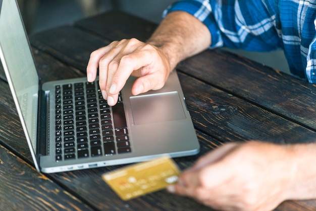 Man's hand holding credit card typing on laptop over the wooden desk