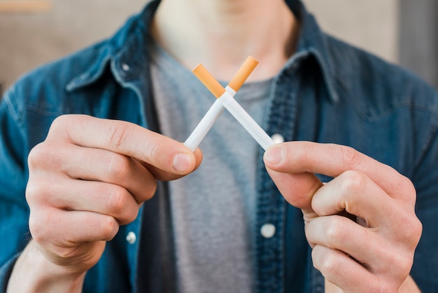 Free photo man's hand holding crossed cigarettes