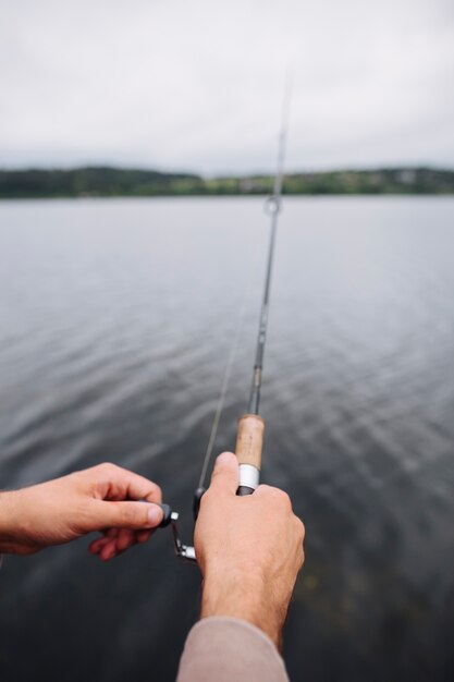 湖の前に釣竿を持っている人間の手