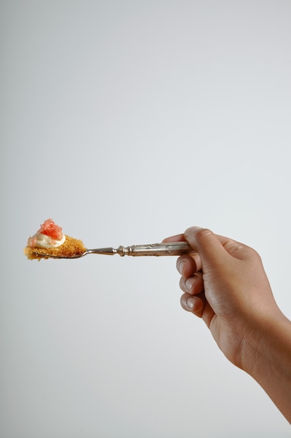 Мужская рука держит вилку с кусочком вкусного бисквита с грейпфрутом, изолированным на белом