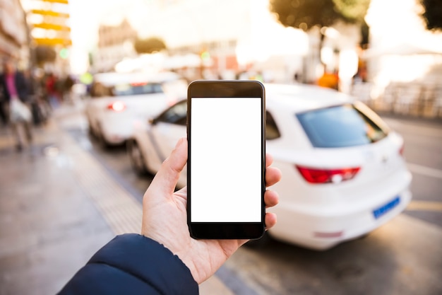 Man's hand holding mobile phone in front of traffic on road