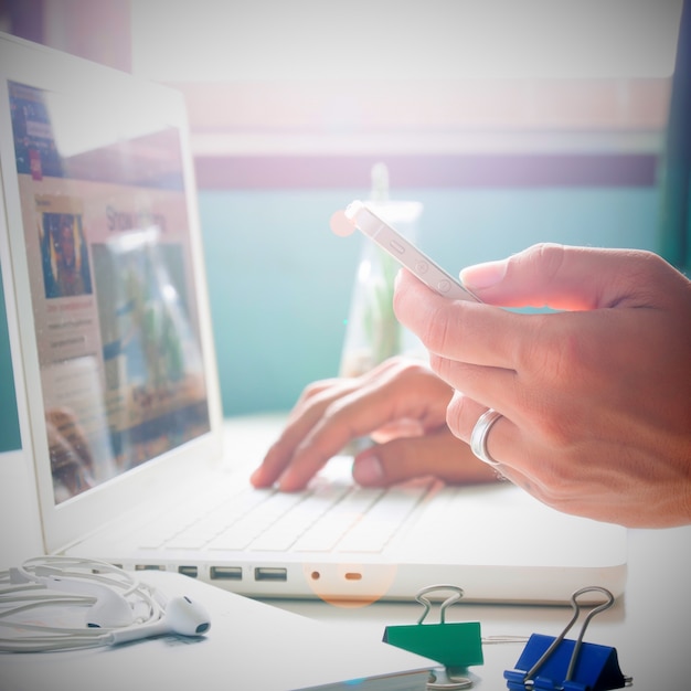 Man's hand holding smartphone and using laptop for online marketing