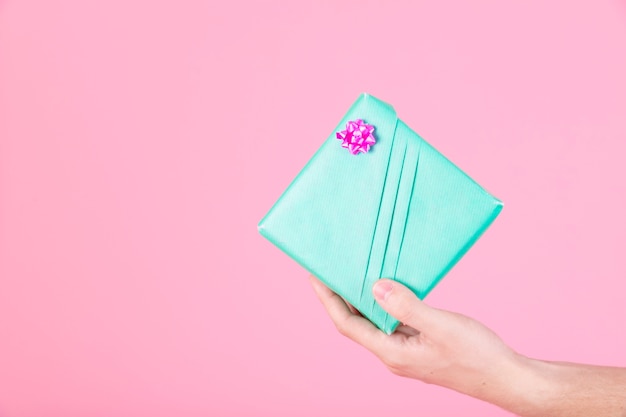 Man's hand holding wrapped turquoise present box on pink background