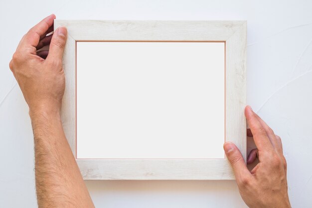 Man's hand placing white picture frame on wall