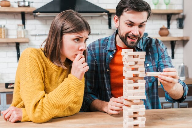 Man's hand taking or putting a block to an unstable and incomplete tower of wooden blocks