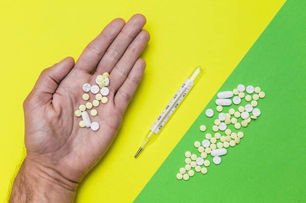 Man's hand with pills near thermometer on dual colored background