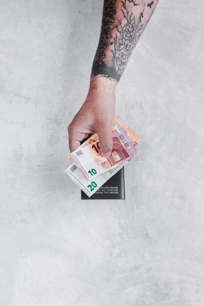 Man's hand with tattoo holding euro notes and passport over the concrete wall