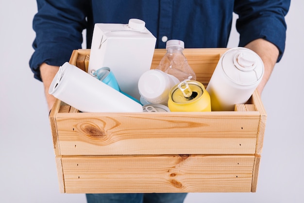 Man's hand with wooden box full of bottles and tin cans