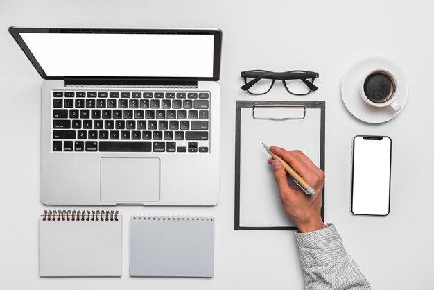 Man's hand writing on clipboard near laptop in office